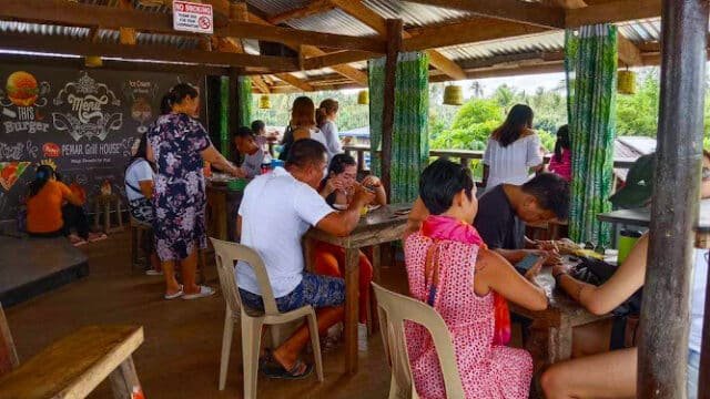 People dining and socializing in an open-air wooden restaurant with colorful decor and natural light in Siargao.