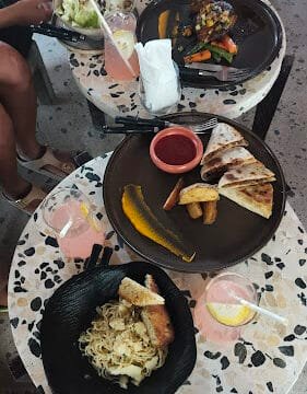 Three plates of assorted food and pink drinks with lemon on terrazzo tables at a Siargao restaurant.