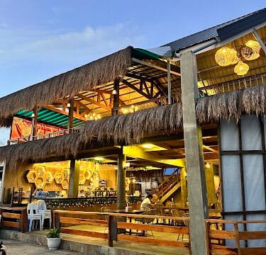 Two-story open-air restaurant with thatched roof and warm lights, viewed at dusk in Siargao.