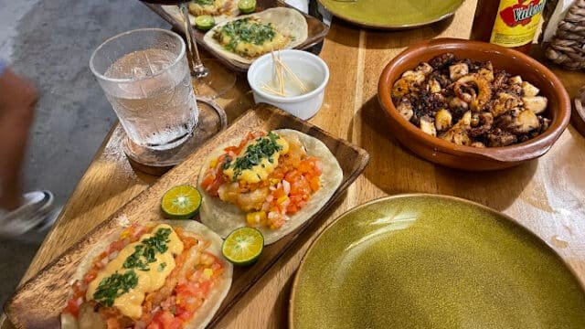 Two plates of tacos, grilled seafood, hot sauce, and drinks on a wooden table in Siargao.