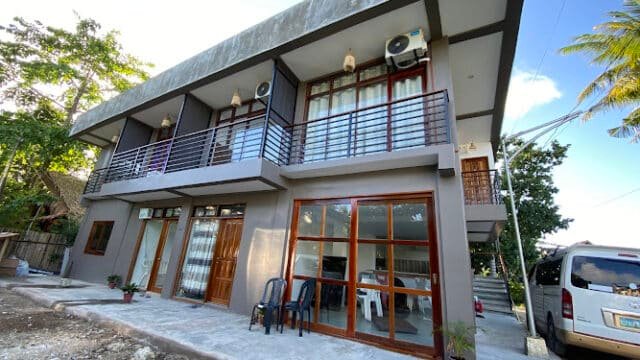 Two-story modern house with balconies and large windows in Siargao, a van parked nearby under a partly cloudy sky.