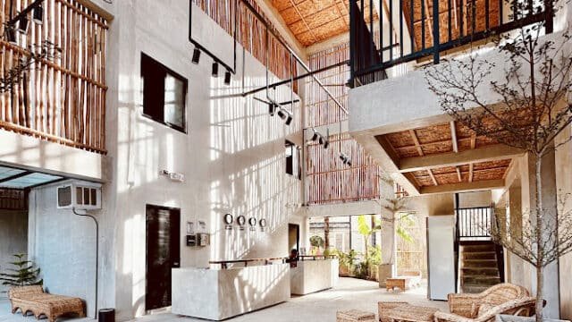 Modern lobby with natural light, rattan furniture, concrete walls, and wooden railings, featuring indoor plants inspired by Siargao.