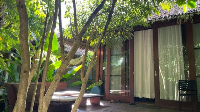 Sunlit wooden patio with lounge chairs, surrounded by lush green trees and plants, evokes the tropical vibe of Siargao.