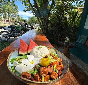 A bowl of rice, tofu, fresh vegetables, and watermelon slices enjoyed outdoors on a sunny day in Siargao.