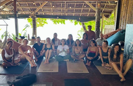 A group of people sit on yoga mats in an open, tropical Siargao thatched-roof space; a black dog rests in front.