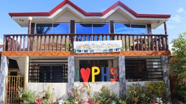 Two-story building with large windows, wooden balcony, and colorful I ♥ PHS letters in the Siargao front garden.