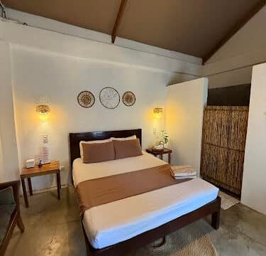 Cozy Siargao bedroom with double bed, brown accents, woven rug, wall art, and warm lighting.