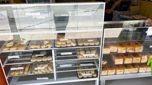 A bakery display case filled with various breads and rolls, with a person standing behind the counter in Siargao.