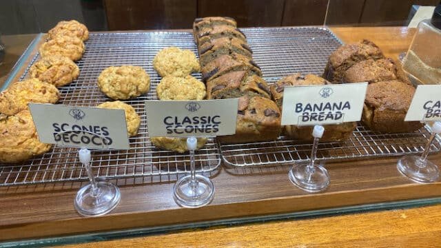 Assorted scones and banana bread on a wire rack display with labeled signs in a cozy Siargao bakery.