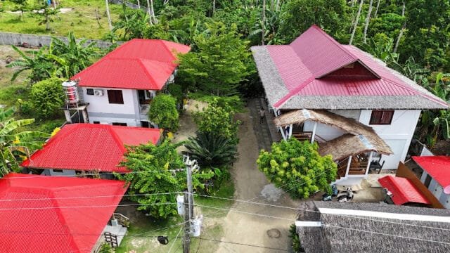 Aerial view of white buildings with red roofs surrounded by lush green trees and vegetation in Siargao.