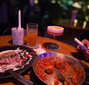 A table with empty dishes, drinks, and a person using a phone in a dimly lit Siargao restaurant.
