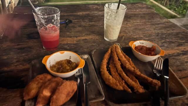Two plates of fried food and dipping sauces with smoothies on a wooden table in Siargao’s cozy outdoor setting at night.