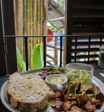 A plate with sliced bread, butter, guacamole, and seasoned meat on a table near a window in Siargao.