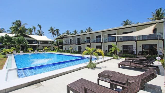 Outdoor pool with wicker lounge chairs, modern hotel buildings, and palm trees under the clear Siargao sky.