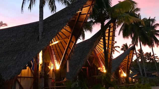 Tropical huts with thatched roofs lit warmly at sunset, surrounded by palm trees on the island of Siargao.