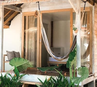 Small wooden porch with a hammock, potted plants, and a bench outside a cozy Siargao house with thatched roof.