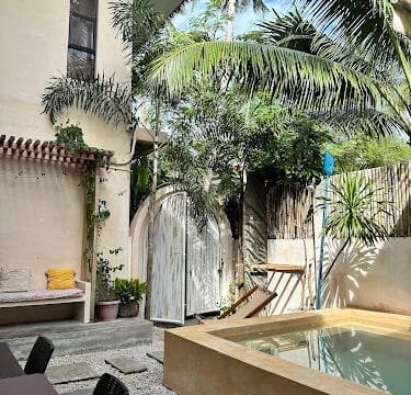 A sunny Siargao courtyard with a small pool, palm trees, a hammock, and a cozy bench with yellow pillows.