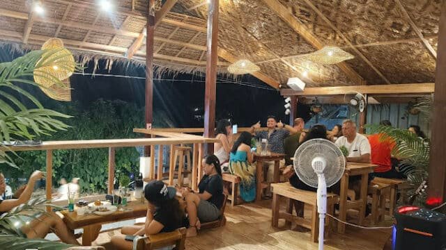 People dining and socializing at a cozy, open-air Siargao restaurant with wooden decor and warm lighting at night.