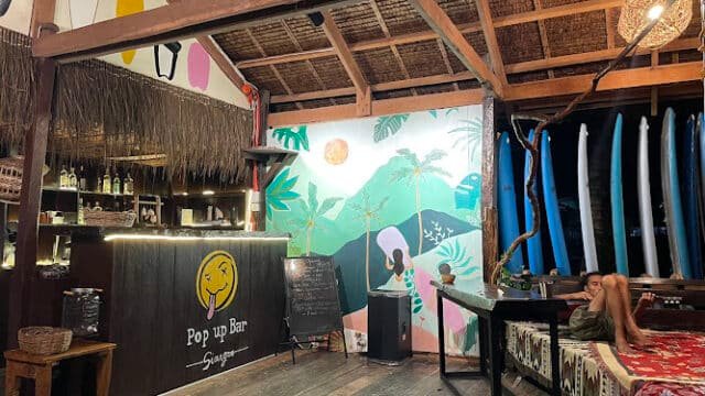 Cozy pop-up bar in Siargao with surfboards, a tropical mural, and a person relaxing on a patterned sofa in a wooden interior.