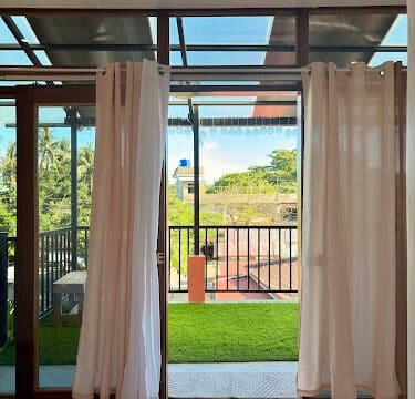Sliding glass doors with white curtains open to a balcony with green artificial grass and outdoor Siargao views.