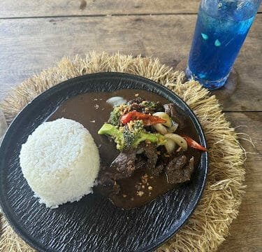 A plate of rice and beef stew with vegetables, served Siargao-style with a blue drink garnished with a lemon slice.