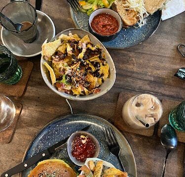 Top-down view of a table in Siargao with nachos, salad and sandwich, burger with fries, drinks, and sauces.