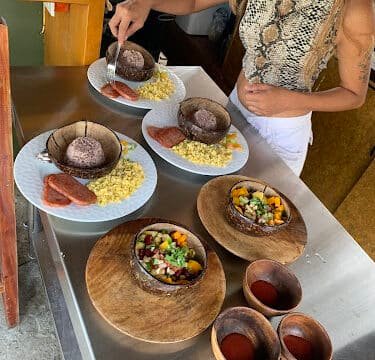 Woman in Siargao plating dishes with rice, eggs, sausage, and salad on a stainless steel countertop.
