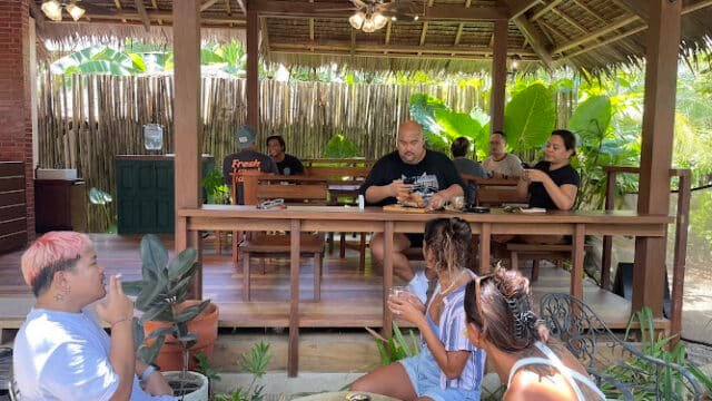 People dining and chatting at an outdoor, rustic Siargao restaurant with wooden furniture and lush green plants.