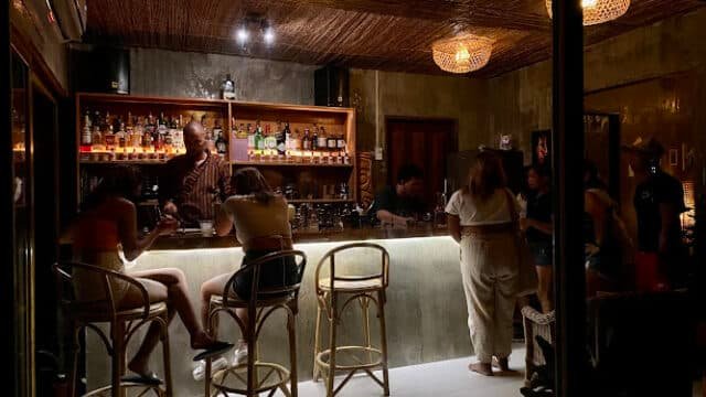 Dimly lit Siargao bar with people at the counter, bartender serving drinks, exuding a warm and cozy atmosphere.