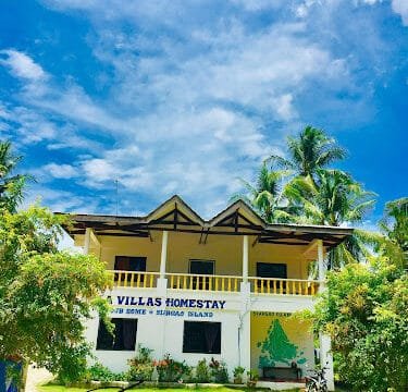 Two-story Siargao homestay under a bright blue sky, surrounded by palm trees and greenery, with a bicycle outside.