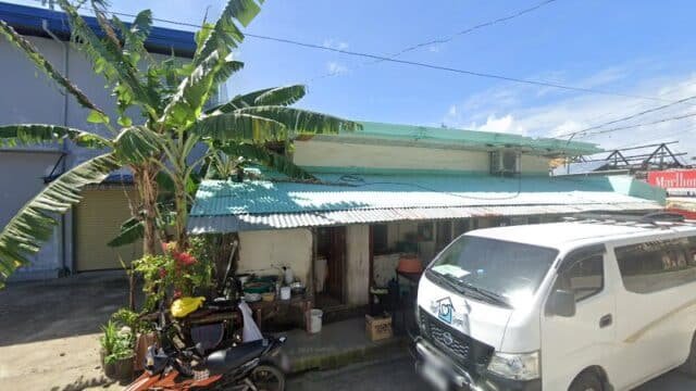 A small roadside house in Siargao with a corrugated metal roof, a banana tree, motorcycle, and white van parked outside.